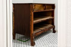 an old wooden shelf sitting in the corner of a room with tile flooring and white walls