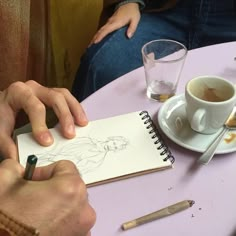 two people sitting at a table with coffee and pencils