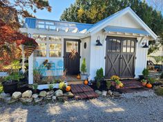 a small house with lots of plants and pumpkins in the front yard on gravel