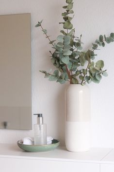 a white vase sitting on top of a table next to a mirror and soap dispenser