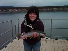 a woman standing on a dock holding a fish