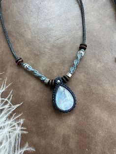 a necklace with a blue tear shaped stone hanging from it's side on a brown leather cord