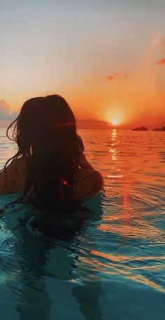 a woman in the water at sunset with her back turned to the camera and looking into the distance