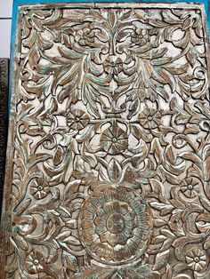 an intricately carved wooden panel with flowers and leaves in the center, sitting on a tile floor