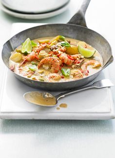 a pan filled with food sitting on top of a white plate next to a silver spoon