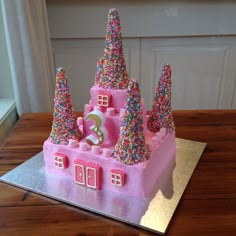 a pink castle cake with sprinkles and a number on the front is sitting on a table