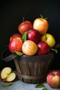 a wooden basket filled with lots of red and yellow apples next to green leafy leaves