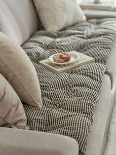 a couch with some food on top of it next to pillows and a window in the background