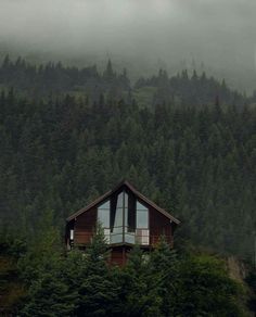 a house on top of a hill with trees in the background and foggy sky