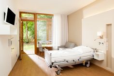 a hospital room with a bed, chair and flat screen tv mounted on the wall