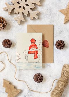 a card with a snowman wearing a red hat and scarf on it next to pine cones