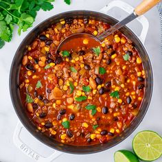 a pot filled with chili and beans next to limes, cilantro and parsley