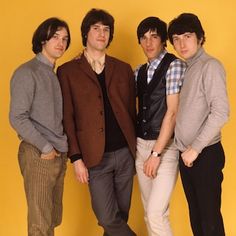 four young men standing next to each other in front of a yellow wall