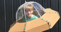 a young boy in a cardboard space ship with an umbrella over his head and blue balls on it