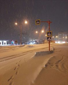 a snow covered street at night with traffic signs and buildings in the background on a snowy day