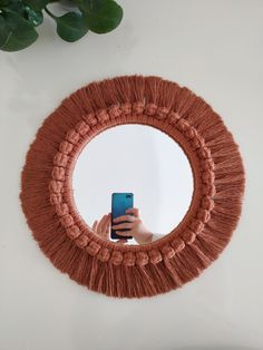 a person holding a cell phone in front of a round mirror with fringed edges