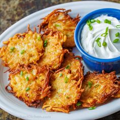 potato pancakes with sour cream and chives on a white plate next to a blue bowl