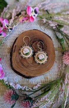 a pair of earrings sitting on top of a piece of wood next to pink flowers