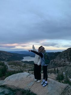 a woman standing on top of a rock with her arms outstretched in front of the camera