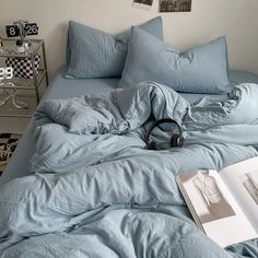 an unmade bed with blue sheets and headphones on the end, next to a book