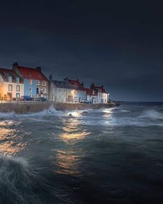 some houses by the water at night with waves crashing in front of them and lights on