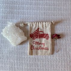 a small drawstring bag sitting on top of a bed next to a flower