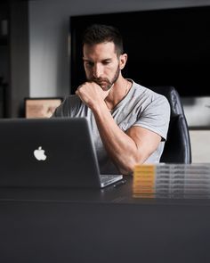 a man sitting in front of a laptop computer on top of a wooden table next to a desk