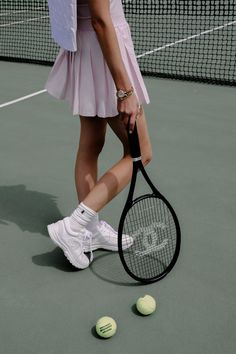 a woman holding a tennis racquet on top of a tennis ball court with two tennis balls