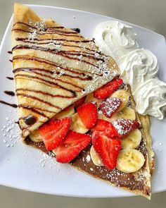 a white plate topped with pancakes covered in whipped cream and sliced strawberries