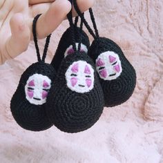 three crocheted black and white toy with pink eyes hanging from it's strings