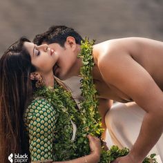 a man and woman kissing each other while surrounded by greenery on their backs, in front of a body of water