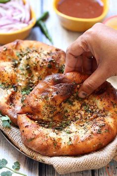 a person is placing herbs on top of a pizza crust with sauces in the background