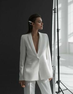 a woman standing in front of a camera wearing a white suit