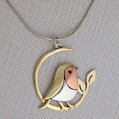 a bird sitting on top of a crescent shaped pendant with a pink and white face