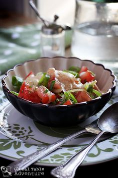 a bowl filled with salad sitting on top of a table next to two spoons