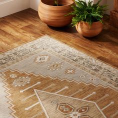 two planters are sitting on the floor next to a beige and white rug with an ornate design