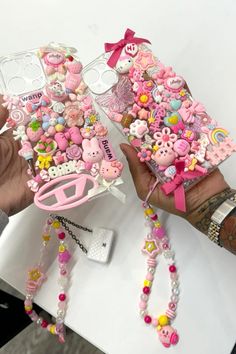 two hands holding up cell phones covered in pink and white buttons, beads, and bows