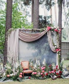 a chair sitting in the middle of a forest filled with flowers and greenery next to a painting