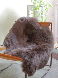 a chair with a fur covering on it in front of a potted plant next to a window