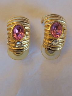 "Beautiful Vintage Gold Metal Hoop Earrings from Givenchy The earrings have gold ridges throughout the earring.  Gold Hoops with a Pink topaz Gemstone and white crystal rhinestone. This vintage pair of glamorous Givenchy clip earrings has an elegant design. Marks: Givenchy  Size: 1\" L x 1/4\" W These earrings are in a good vintage condition. SPECIAL NOTE: The post backing closure is yellowed from wear. The actual earring and post attached to the earring are in good shape. You can use other post Vintage Givenchy, Jeweled Earrings, Pink Topaz, Topaz Stone, Gold Hoops, Gold Hoop, Topaz Gemstone, Gold Hoop Earrings, Jewelry Earrings Hoops