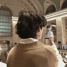 a woman taking a photo with her cell phone in a train station, while wearing a sweater