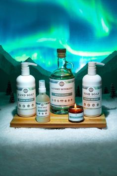 three bottles and two candles sitting on a tray in front of an aurora display with northern lights