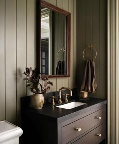 a bathroom sink sitting under a mirror next to a white toilet and wooden cabinets with gold faucets