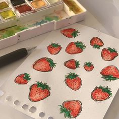 a drawing of strawberries on a sheet of paper next to watercolor paints and a brush