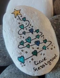 a rock with a christmas tree painted on it sitting next to some rocks and candles