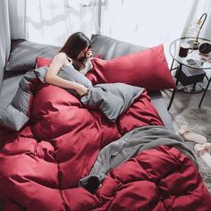 a woman is laying in bed with red comforter and pillows on her stomach, talking on the phone