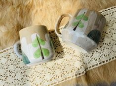 two coffee mugs sitting on top of a lace doily next to each other