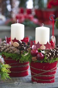 two red pots filled with pine cones and white candles sitting on top of a table