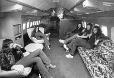 black and white photo of people sitting in an airplane with their feet on the couches