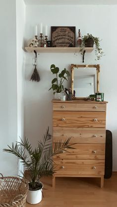 a wooden dresser sitting on top of a hard wood floor next to a mirror and potted plant